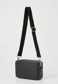 Sac bandoulière noir rectangulaire en matériau texturé, avec une fermeture éclair et une sangle en nylon réglable.