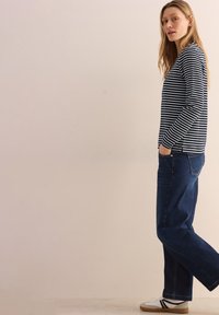 Gestreiftes Langarmshirt in Marineblau und Weiß, kombiniert mit dunkelblauen Jeans und weißen Sneakers mit schwarzen Akzenten. Lässige Passform und weicher Stoff.
