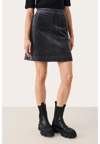 Jupe A-line en velours côtelé gris avec une taille ajustée et une texture verticale subtile, associée à des bottines noires chunky.