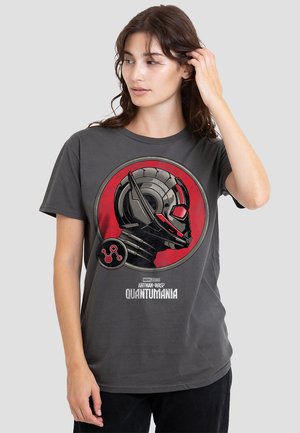 Woman with brown hair wearing a dark gray Ant-Man and the Wasp: Quantumania T-shirt featuring a red and black helmet design.