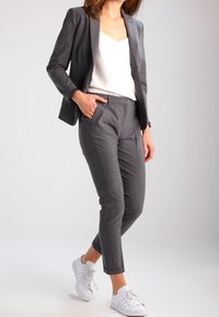 Blazer a quadri grigi con silhouette aderente, abbinato a pantaloni slim-fit coordinati e sneakers bianche. Tessuto liscio, linee pulite, design minimalista.