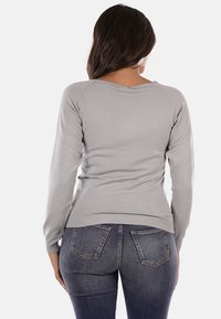 Maglione grigio chiaro a maniche lunghe con vestibilità comoda, texture a costine e scollatura a V, abbinato a jeans blu scuro con tasche posteriori.