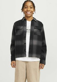 Mustra musternuu mustri ja halli flanellshirt, millel on kaks rinnataskut, nööbiklapp ja pikad varrukad, kantud valge graafilise t-särgi ja beežide pükstega.