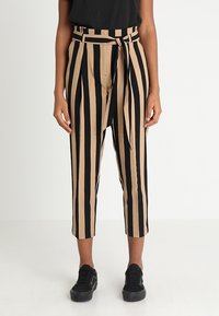 Paskowe spodnie w czerni i beżu, z wysokim stanem i przewiązanym paskiem, krótkiej długości, z kieszeniami po bokach. Noszone z czarnymi sneakersami.