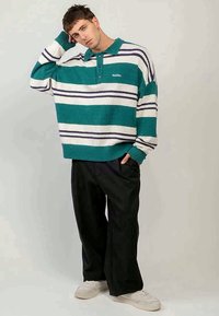 Randig tröja i teal, vitt och marinblått med krage och knappar. Bärs med lösa svarta byxor och vita sneakers, med en mjuk textur.