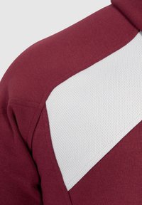 Sudadera burdeos con un panel de malla blanca; presenta un tejido texturizado y un diseño deportivo, resaltando un patrón de bloques de color.