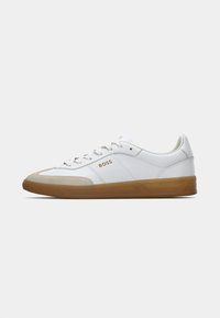 Vita lädersneakers med beige mocka tåhätta, gummisulor och en gyllene "BOSS"-logotyp på sidan. Platta snören och minimalistisk design.