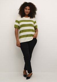 Stribet sweater i creme og olivengrøn, korte ærmer, afslappet pasform, parret med sorte tætsiddende bukser og sorte spidse sko.