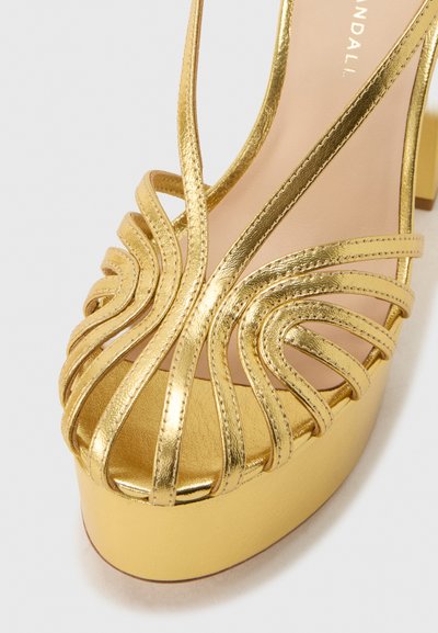 Χρυσό σανδάλι πλατφόρμα με ψηλό τακούνι και λεπτά μεταλλικά λουράκια πάνω από τα δάχτυλα και το τακούνι, κοντινή λήψη.