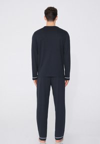 Conjunto de ropa de estar para hombre en azul marino, que incluye mangas largas y pantalones con ribete blanco. Tela suave, ajuste relajado, diseño minimalista.