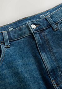 Jean en denim bleu avec fermeture à boutons, passants pour ceinture, taille 34R, étiqueté coupe baggy et style jambe large.