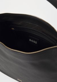 Borsa a tracolla in pelle nera con una cerniera in tonalità oro, interno foderato e tasca interna. Presenta un'etichetta di marca visibile con la scritta "BOSS."