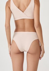 Beżowy, bezszwowy biustonosz bez fiszbin i pasujące figi, wykonane z miękkiej, elastycznej tkaniny. Biustonosz ma krzyżujący się design pleców.