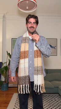 Ull skjerf med vekslende beige, brune og krem-striper, avsluttet med lange frynser, brukt over en blå stripete skjorte med knapper.