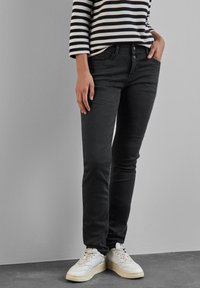 Svarta jeans i slim fit med fem fickor och knäppt gylf. Kombinerat med ljusa sportskor. Randig topp synlig.