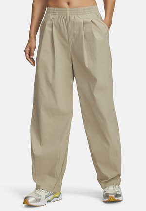 Pantalons larges beiges avec une taille élastique et des plis avant, fabriqués dans un tissu lisse. Assortis à des baskets de couleur claire.