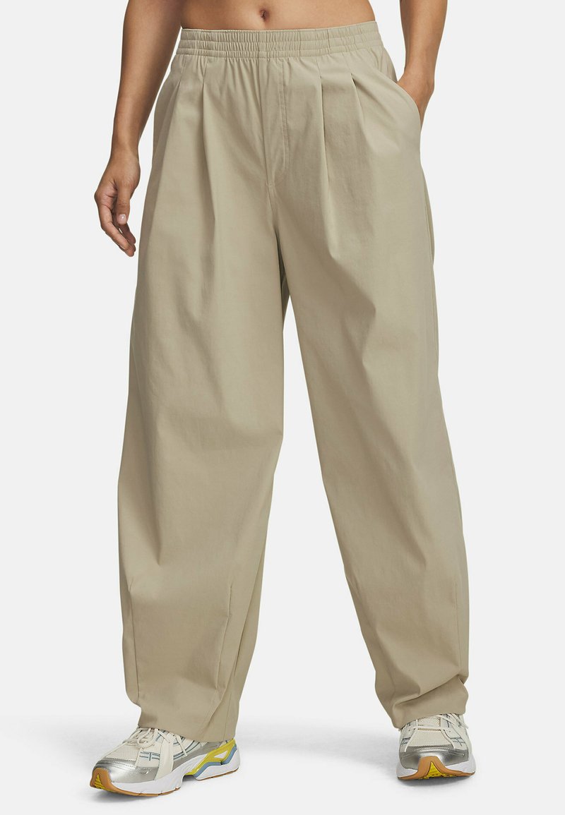 Beige leveleggsbukser med strikk i livet og frontfolder, laget av glatt stoff. Kombinert med lyse joggesko.