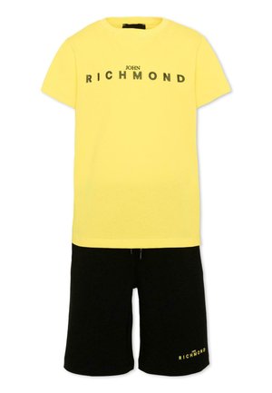 T-shirt jaune à manches courtes avec le texte « John Richmond » associé à un short noir avec un petit texte « John Richmond » sur la jambe gauche.