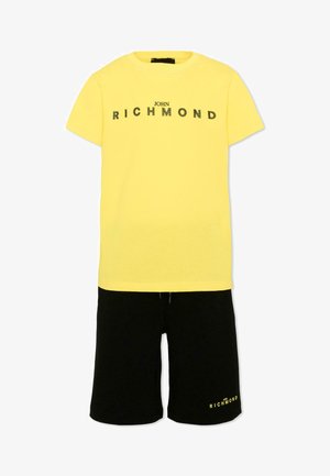 Geel T-shirt met korte mouwen met de tekst "John Richmond" gecombineerd met zwarte shorts met kleine "John Richmond" tekst op het linkerbeen.