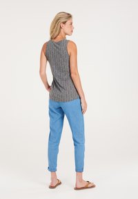 Top senza maniche grigio a fantasia con scollatura rotonda, abbinato a jeans azzurri con risvolto e sandali marroni, visto da dietro.