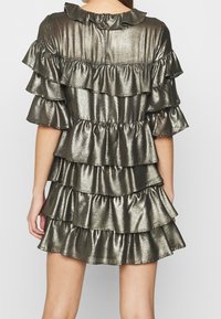 Metallinen mekko, jossa on useita kerroksittain olevia volyymeja, rypytetty kaula-aukko, lyhyet hihat ja takana avaus avaimenreikänä tummassa hopeasävyssä.