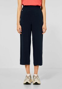 Marina korta byxor med elastisk midja, lätt tyg, vida ben och sidslitsar vid fållen, i kombination med beige sneakers.