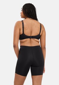 Soutien-gorge sans fil noir avec bretelles ajustables et short taille haute assorti. Texture lisse, coutures minimales et design sans couture au niveau de la taille.