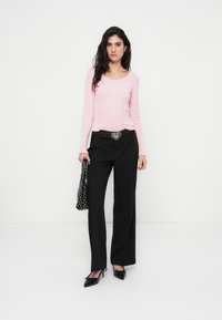 Ανοιχτό ροζ ριμπ μακρυμάνικη μπλούζα, μαύρο παντελόνι φαρδύ με ασημένια αγκράφα σε σχήμα καρδιάς στη ζώνη, μαύρες γόβες slingback και μαύρη τσάντα με πουά σχέδιο.