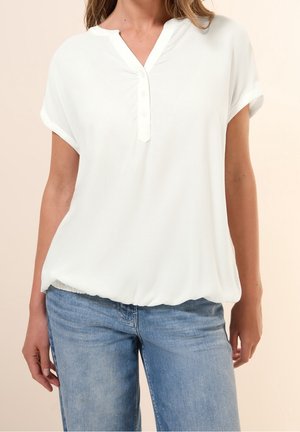 Witte blouse met korte mouwen, een V-hals en een knopenbies. Zachte, lichtgewicht stof met een geplooide zoom, gecombineerd met lichtblauwe spijkerbroek.