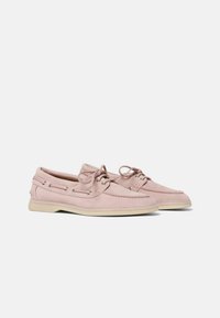 Zapatos de barco de ante rosa claro con suela de goma beige, detalles de cordones y ojales de metal. Punta redondeada y acentos cosidos.