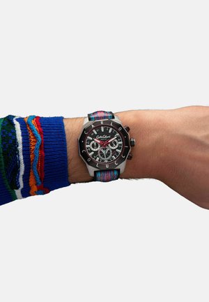 Schwarze Chronograph-Uhr mit einem Gehäuse aus silbernem Edelstahl, ausgestattet mit einem bunten Stoffarmband mit abstrakten Mustern, das an einem Handgelenk präsentiert wird.