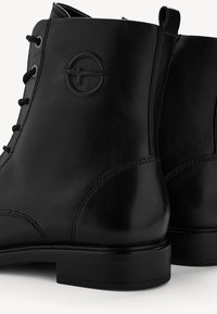 Bottines en cuir noir avec détail lacé, logo rond embossé sur le côté et languettes à l'arrière.