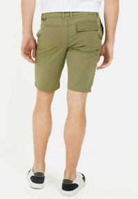Khaki-Shorts mit geradem Schnitt, zwei Gesäßtaschen und seitlichen Schlitzen. Kombiniert mit weißen und marineblauen Sneakers. Glattes Baumwoll-Mix-Gewebe.