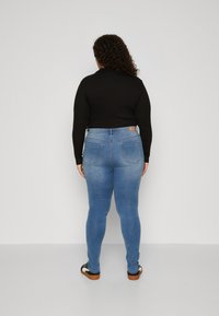 Μπλε τζιν skinny παντελόνι με ψηλή μέση, πίσω τσέπες και ανοιχτό χρώμα. Συνδυασμένο με μαύρο τοπ με μακριά μανίκια και μαύρες σαγιονάρες.