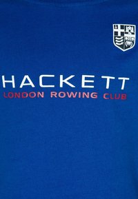 Blå bomullströja med "HACKETT" i vitt, "LONDON ROWING CLUB" i rött och en liten sköld på övre vänster sida. Slät, tät passform.
