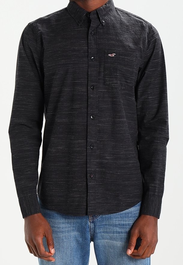 Svart långärmad skjorta med knapp-ner krage, texturerat tyg, subtila streck och en liten logotyp på vänster bröst.