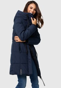 Navy blue puffer coat with a high collar, zip closure, and drawstring at the waist. Features a quilted pattern and black accents.