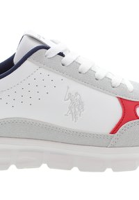 Scarpa da ginnastica bianca con accenti in suede grigio, dettagli rossi, lato perforato e suola testurizzata. Include logo sul lato e lacci bianchi.