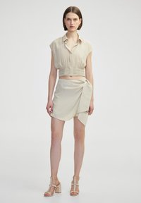 Beige cropped shirt met kraag en geplooide details, gecombineerd met een bijpassende wikkelrok met een zijstrik. Glad, lichtgewicht stof.