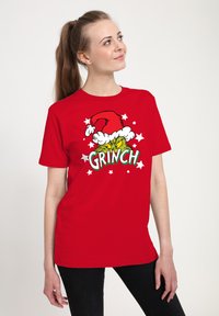 Červené tričko s krátkým rukávem s motivem Zeleného Grinche v santovské čepici, zdobené bílým umělým kožíškem a hvězdami.