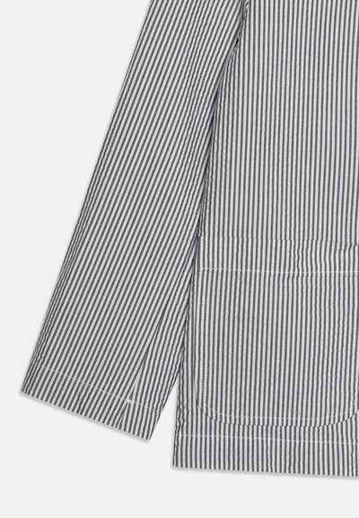 Manche longue avec fines rayures verticales noires et blanches et une grande poche avant avec une couture incurvée en bas.