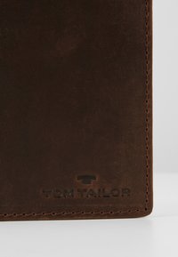 Hnědá kožená peněženka s hladkým povrchem, se značkovým embosovaným logem "TOM TAILOR" a kontrastním prošíváním na okrajích.