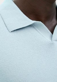 Lyseblå strikket polo skjorte med flad krave og v-hals, der har en tekstureret stof og rene sømme. Ingen synlig hardware eller mønstre.