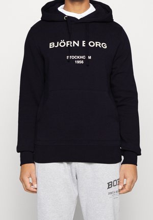 Sudadera negra hecha de tela suave, con un bolsillo tipo canguro, letras en crema en la parte frontal, capucha grande y puños y dobladillo de canalé.