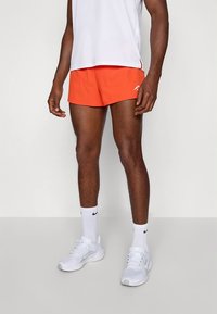 Meeste eredates oranžides spordipükstes valmistatud kergest kangast. Komplektis valge varrukateta särk ja valged tossud mustade detailidega.