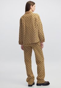 Braun gemusterte Jacke und Hose aus strukturiertem Stoff. Das Outfit zeigt ein Rautenmuster und kontrastierende braune Akzente an Kragen und Saum.