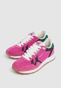 Paire de baskets en daim et mesh rose et noir avec des lacets blancs, des semelles beiges et des accents verts au talon sur un fond gris clair.