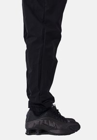 Zapatilla deportiva negra con parte superior texturizada y suela de goma, combinada con pantalones negros ajustados que cuentan con puños elásticos en los tobillos.