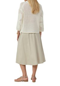 Cremfarbener, offener Strickcardigan mit drei Viertelärmeln, kombiniert mit einem beigen Midikleid und silbernen Riemchen-Sandalen. Glatte Textur, lockere Passform.