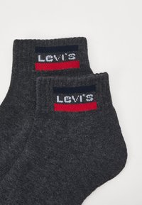 Graue Baumwollsocken für den Knöchel mit einem dunkelblauen und roten gestreiften Logo-Band, auf dem "LEVI'S" steht. Der Stoff hat eine glatte Textur.